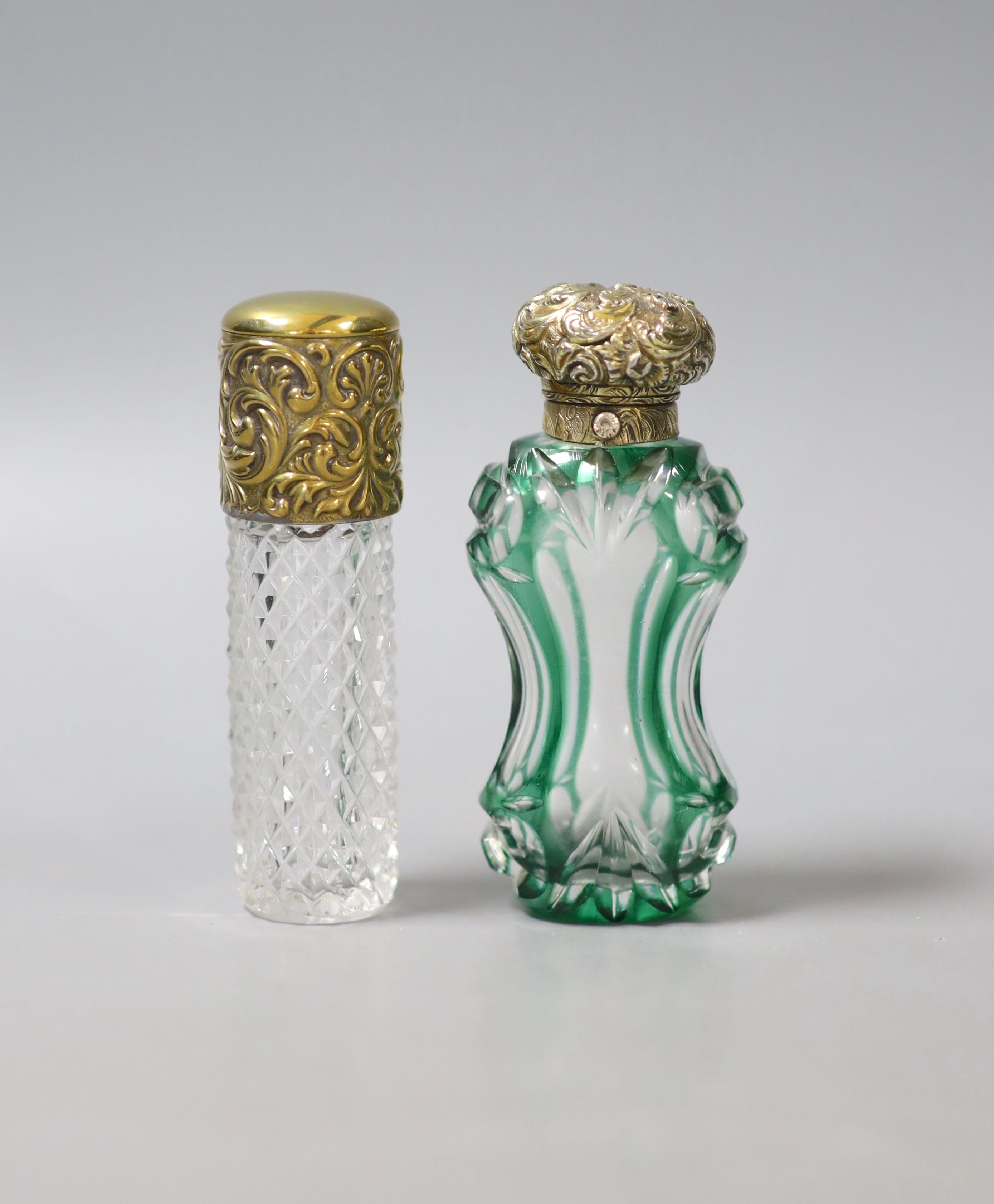 A late Victorian repousse gilt white metal mounted green and clear glass waisted scent bottle, 86mm and one other gilt metal mounted glass scent bottle.